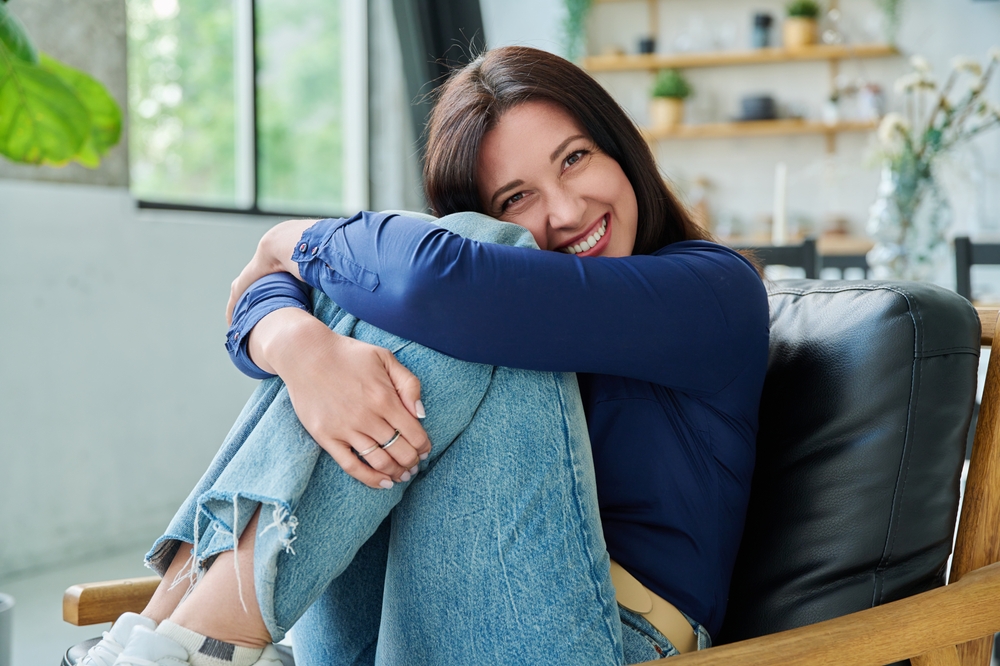 Laughing woman hugging her knees in an armchair
