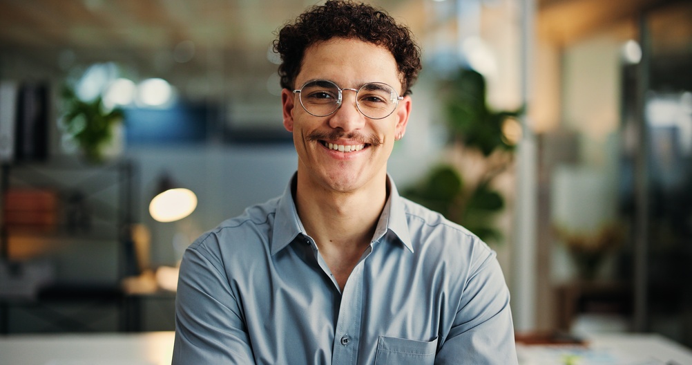Smiling young man with curly hair and glasses in a light blue shirt