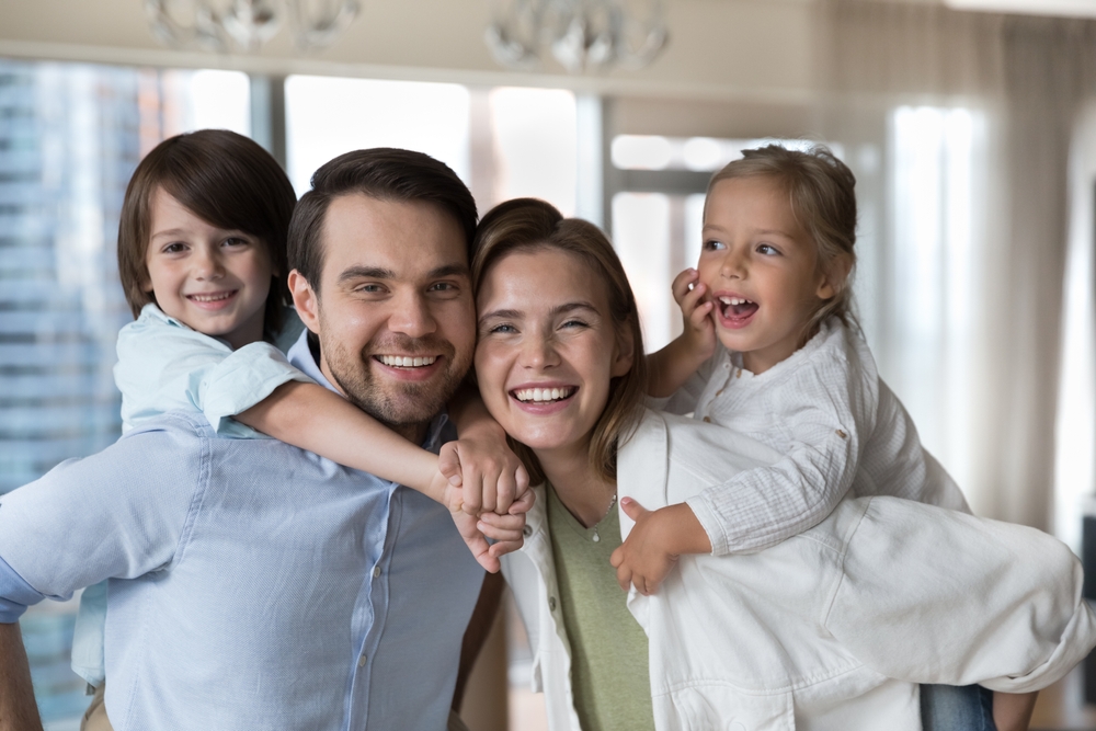 A smiling family of four, the children riding piggyback on their parents