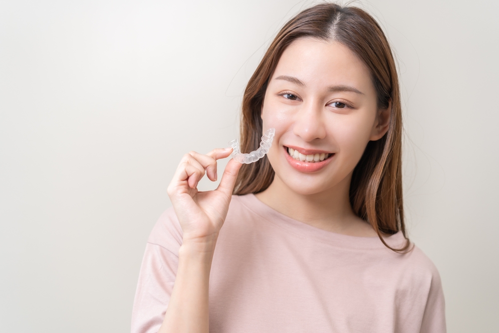 A smiling young woman holding a clear aligner